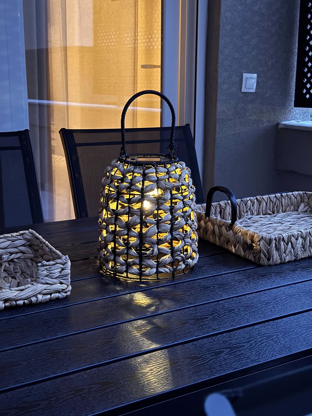 A woven lantern on a table with a chair and a woven basket.