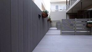Ένας στενός διάδρομος με έναν γκρίζο τοίχο, μια μεταλλική πύλη και κρεμαστές γλάστρες.