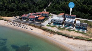 An aerial view of a coastal property with multiple buildings, a beach with umbrellas, and a sign indicating 'NIKOLAOS MARE.' - NikolaosMare  (Nea Propontida)