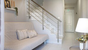 A modern hotel room with a white sofa, a staircase with metal railings, and a bedside table with a lamp. - NikolaosMare  (Nea Propontida)