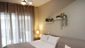 A hotel room with a bed, bedside table, lamp, and wall-mounted shelf with decorative items. - NikolaosMare  (Nea Propontida)
