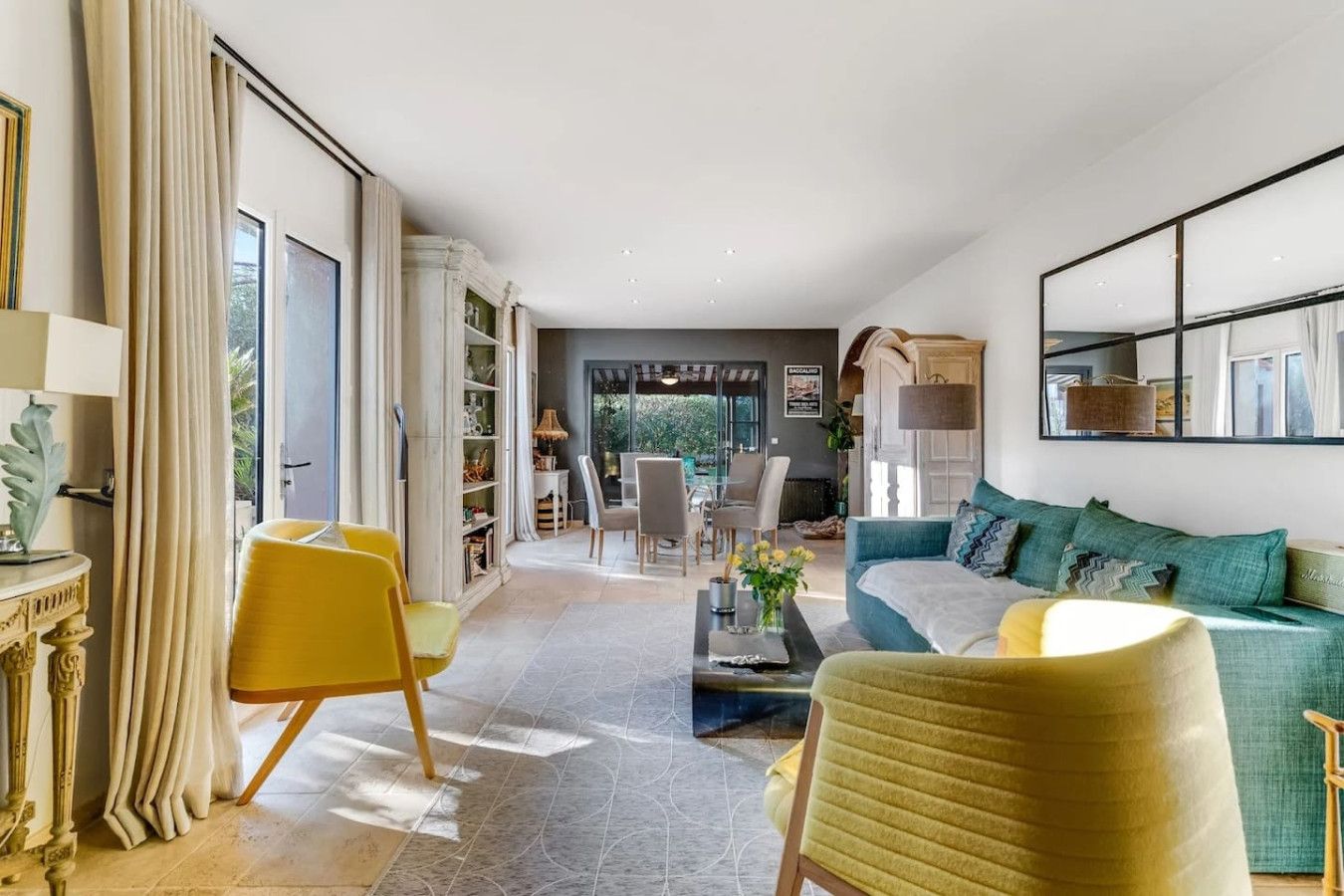 Een moderne woonkamer met een bank, gele fauteuils, een salontafel en een boekenkast.