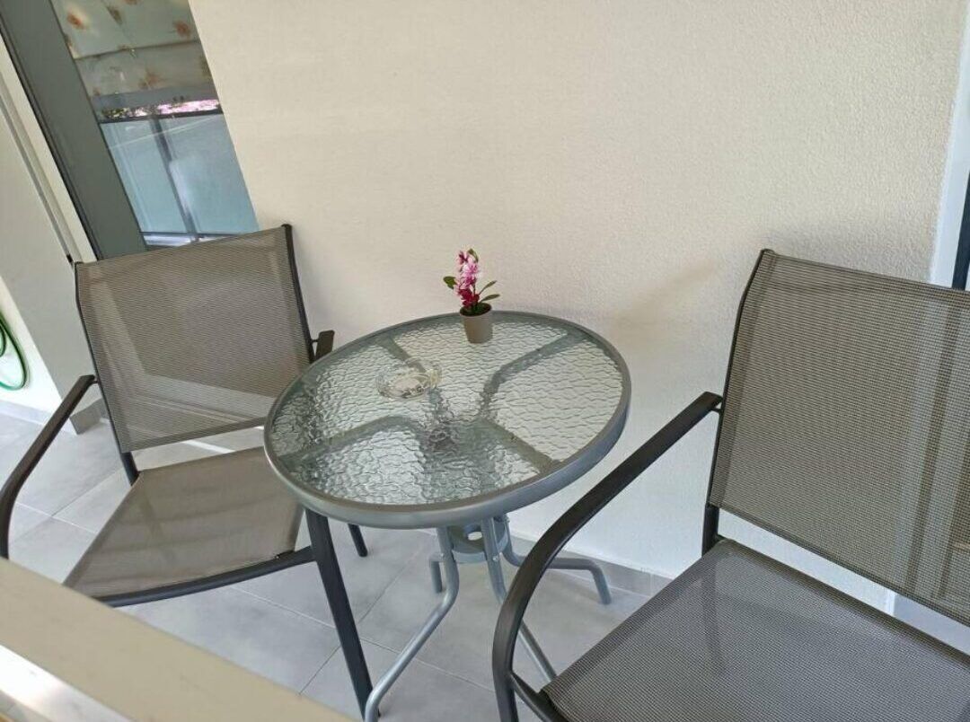 A round glass table with two mesh chairs, a small potted plant, and a view of a balcony.