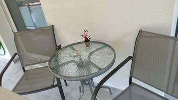 A round glass table with two mesh chairs, a small potted plant, and a view of a balcony.
