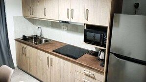 Eine kleine Küche mit Holzschränken, einem Edelstahlkühlschrank, einer Mikrowelle und einem Spülbecken.