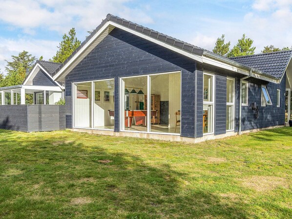Une maison moderne avec une grande entrée en verre, un patio couvert et une pelouse bien entretenue.