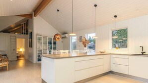 A modern kitchen with white cabinetry, a central island, pendant lighting, and a view of the outdoors. - 5 Star Holiday Home in Blokhus (Blokhus)