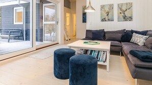A modern living room with a gray sofa, a white coffee table, and two blue ottomans. There are two paintings on the wall and a ladder in the background. - 5 Star Holiday Home in Blokhus (Blokhus)