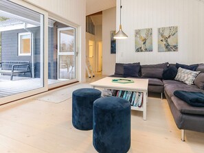 Ein modernes Wohnzimmer mit einem grauen Sofa, einem weißen Couchtisch und zwei blauen Hocker. An der Wand hängen zwei Gemälde, im Hintergrund ist eine Leiter zu sehen.