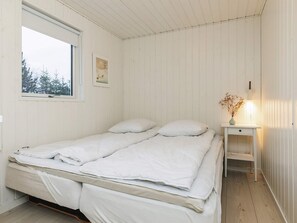 A single-bed room with a wooden floor, a bedside table with a lamp, and a window with a view of trees. - 5 Star Holiday Home in Blokhus (Blokhus)