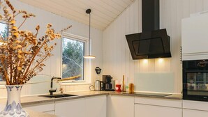 A modern kitchen with white cabinetry, a built-in oven, and a window providing natural light. - 5 Star Holiday Home in Blokhus (Blokhus)
