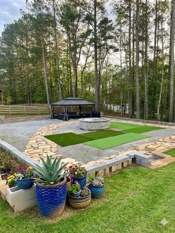 A backyard with a stone patio, a small gazebo, and a lawn with artificial grass.