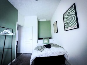 Ein Schlafzimmer mit einem Bett, einem Kleiderständer und einem gerahmten Bild an der Wand.