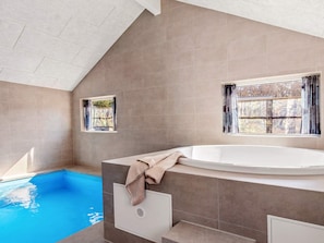 Ein modernes Badezimmer mit einer eingebauten Badewanne, einem kleinen Fenster und einem Pool.