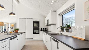 Ett modernt kök med vita skåp, en svart bänkskiva och ett fönster som ger utsikt över omgivningen.