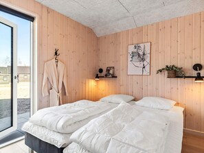 A bedroom with two beds, wooden walls, a window, a hanging robe, wall-mounted lamps, and a framed artwork. - 5 Star Holiday Home in Glesborg (Glesborg)