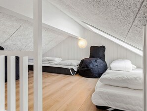 Une chambre à coucher aménagée dans un espace mansardé, avec un plafond en pente, un fauteuil en forme de poire, deux lits et un luminaire fixé au mur.