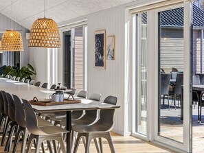 A modern dining area with a long table, chairs, pendant lights, and a view through glass doors. - 5 Star Holiday Home in Glesborg (Glesborg)