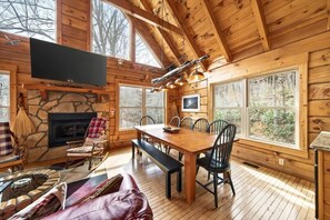 Ein rustikales Blockhaus-Interieur mit Kamin aus Naturstein, einem Holzespeisesaal und großen Fenstern.