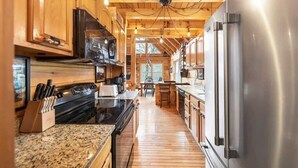 Une cuisine dotée de meubles en bois, d’appareils électroménagers en acier inoxydable, de plans de travail en granit et d’un plancher en bois.