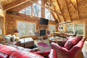 Ein Holzblockhaus-Interieur mit Kamin, Sitzecke, Esstisch und großen Fenstern.