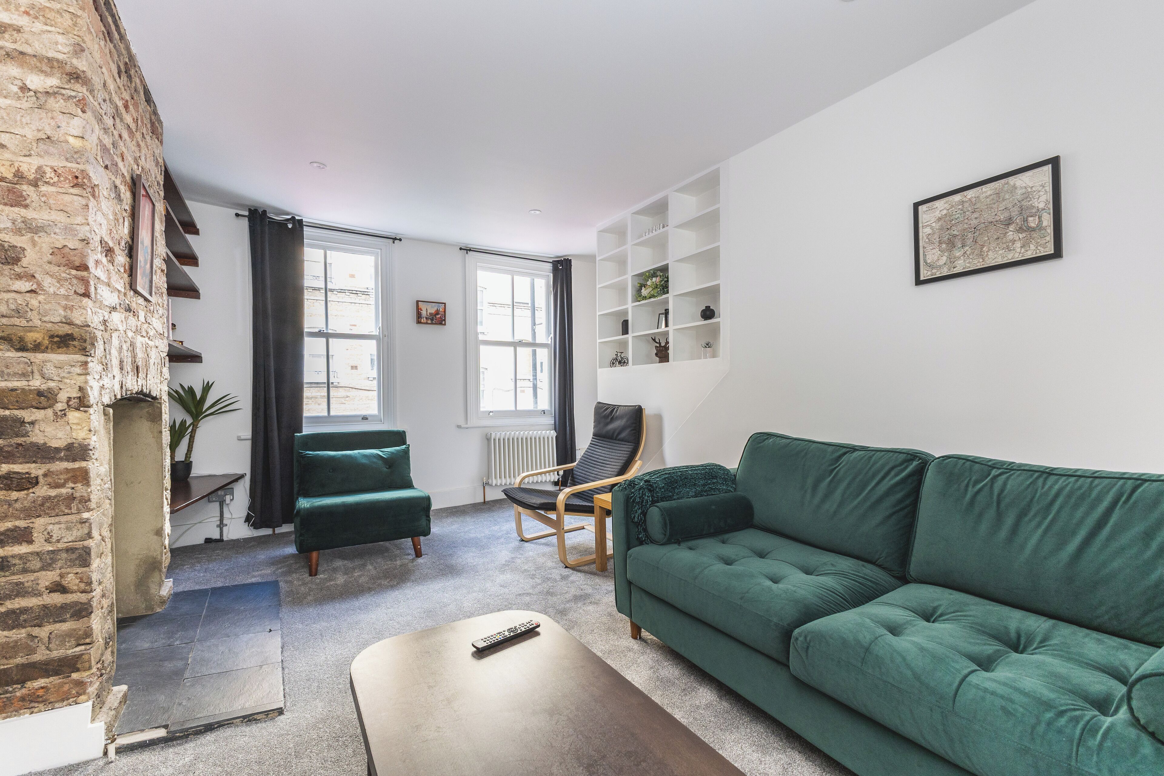 A living room with a green sofa, a wooden coffee table, a black chair, and a brick wall.