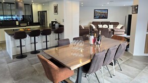 Une cuisine moderne dotée d’un îlot central, de tabourets de bar et d’un coin repas avec une table et des chaises en bois.