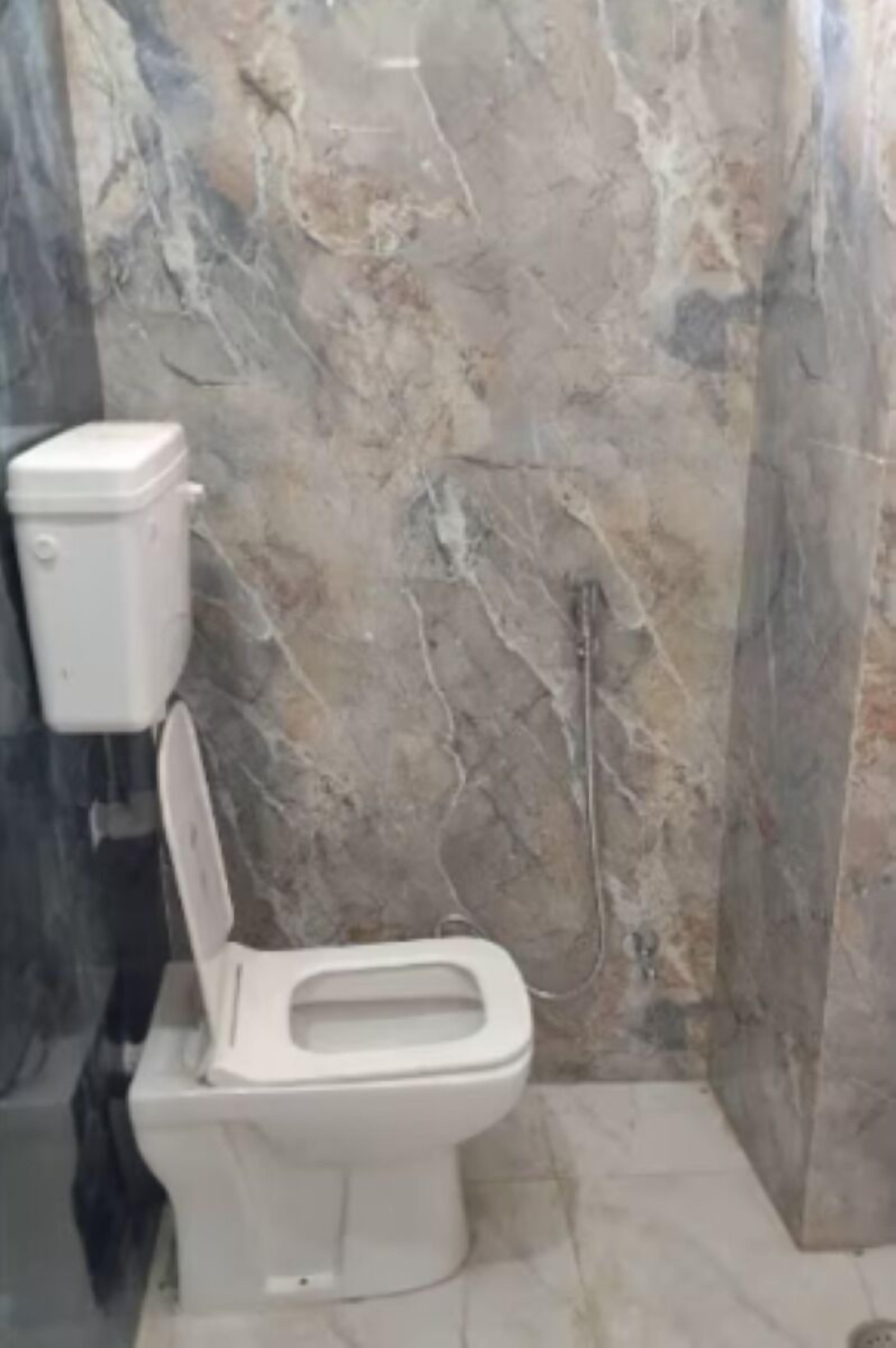 Un bagno con il water, pareti in marmo e un elemento idraulico a vista.