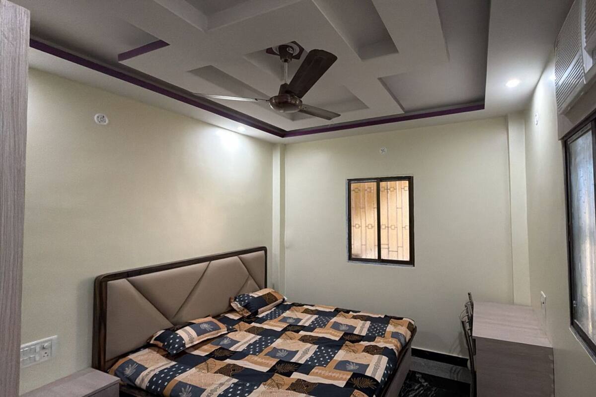A bedroom with a bed, a ceiling fan, a window, and a small table.
