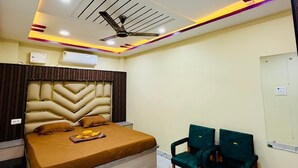 A hotel room with a bed, two chairs, a ceiling fan, and recessed lighting. - Amantran Palace (Mohania)