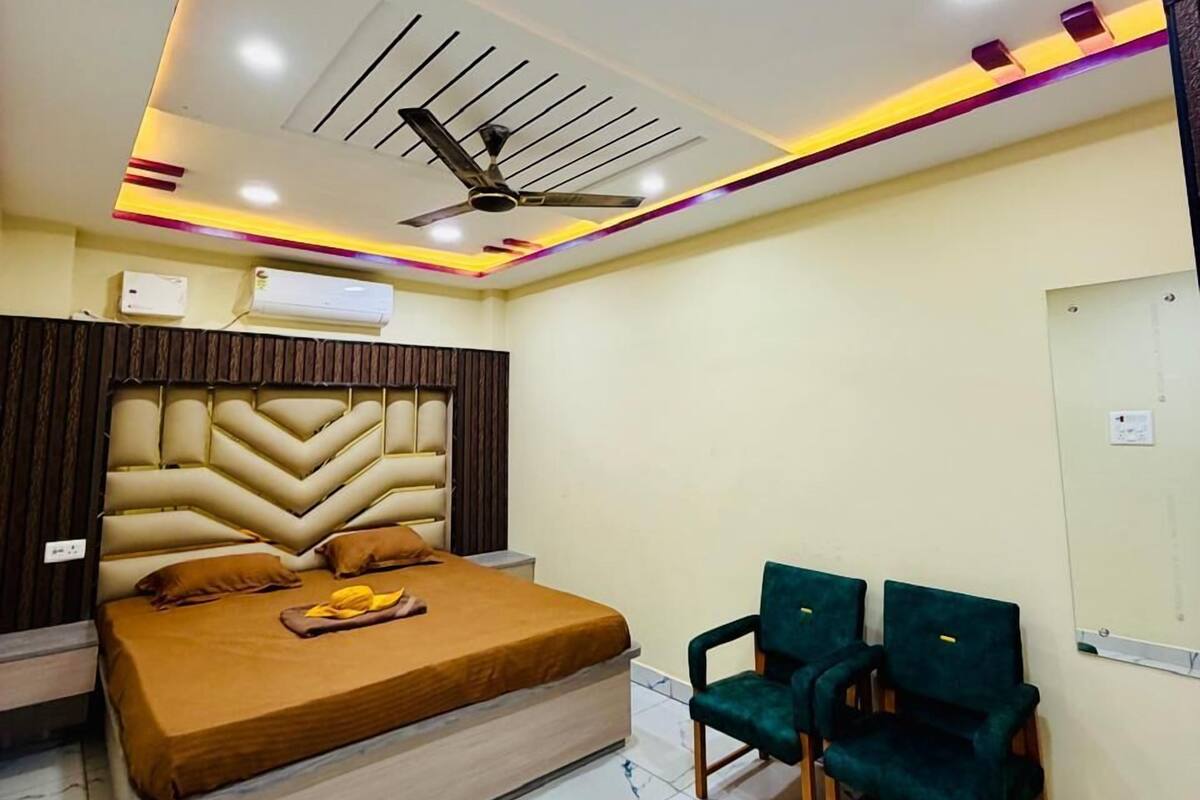 A hotel room with a bed, two chairs, a ceiling fan, and recessed lighting.