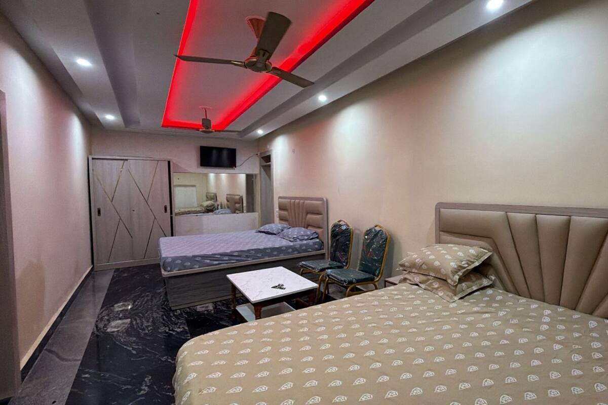A hotel room with a bed, a desk, two chairs, a ceiling fan, and a TV.