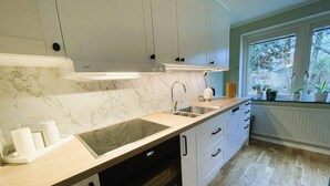 A modern kitchen with white cabinets, a marble backsplash, a black induction cooktop, and a window with plants. - 4 Star Holiday Home in Alingsas (Alingsas)