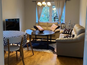 A living room with a sofa, a dining table with chairs, a TV, and a window with curtains. - 4 Star Holiday Home in Alingsas (Alingsas)