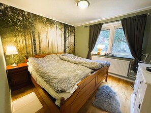 Un dormitorio con cama, mesita de noche, lámpara, ventana con cortinas y radiador.