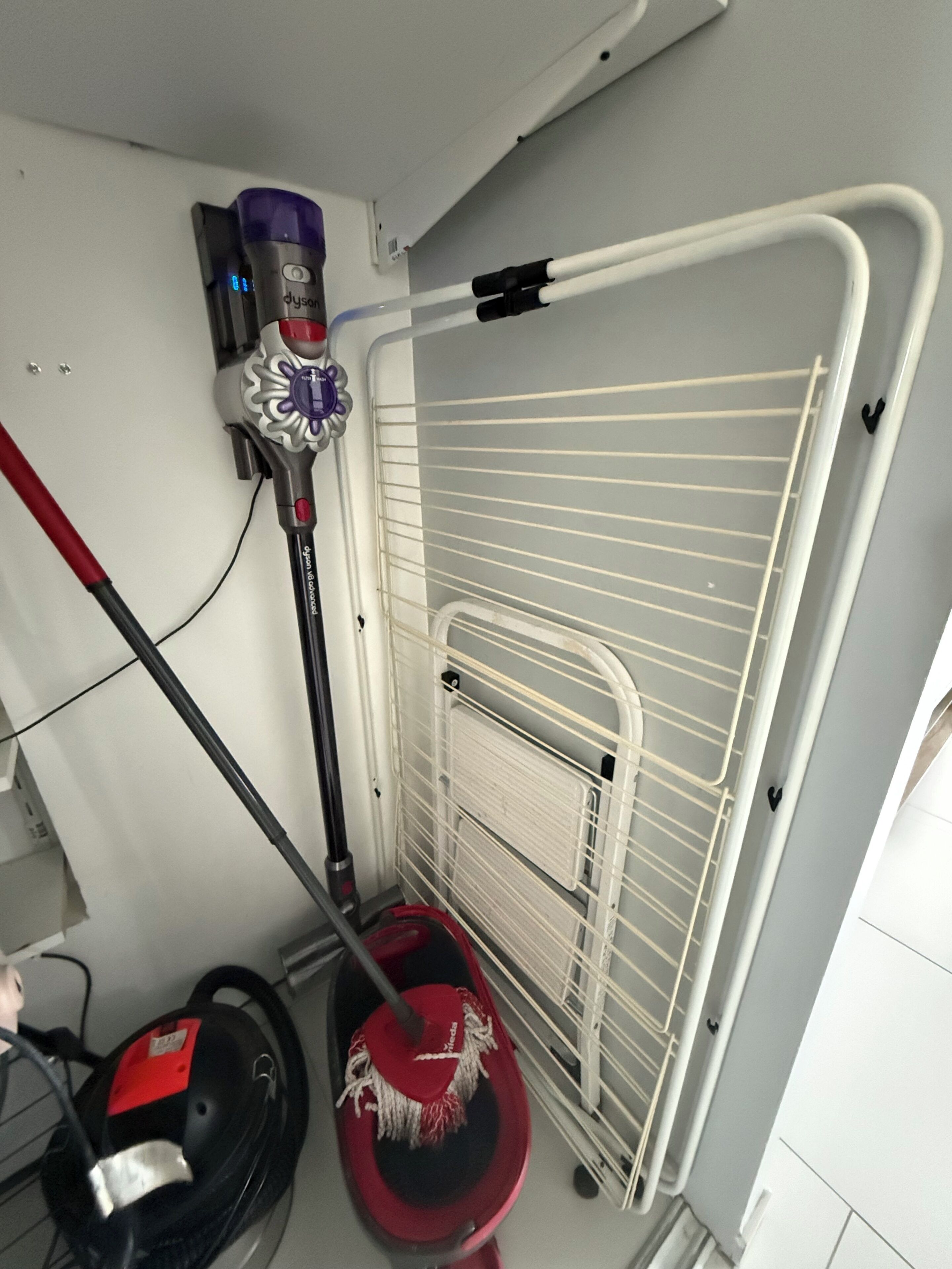 Et hjørne af et rum med en hvid radiator, en hvid metalkasse og en rød moppe.