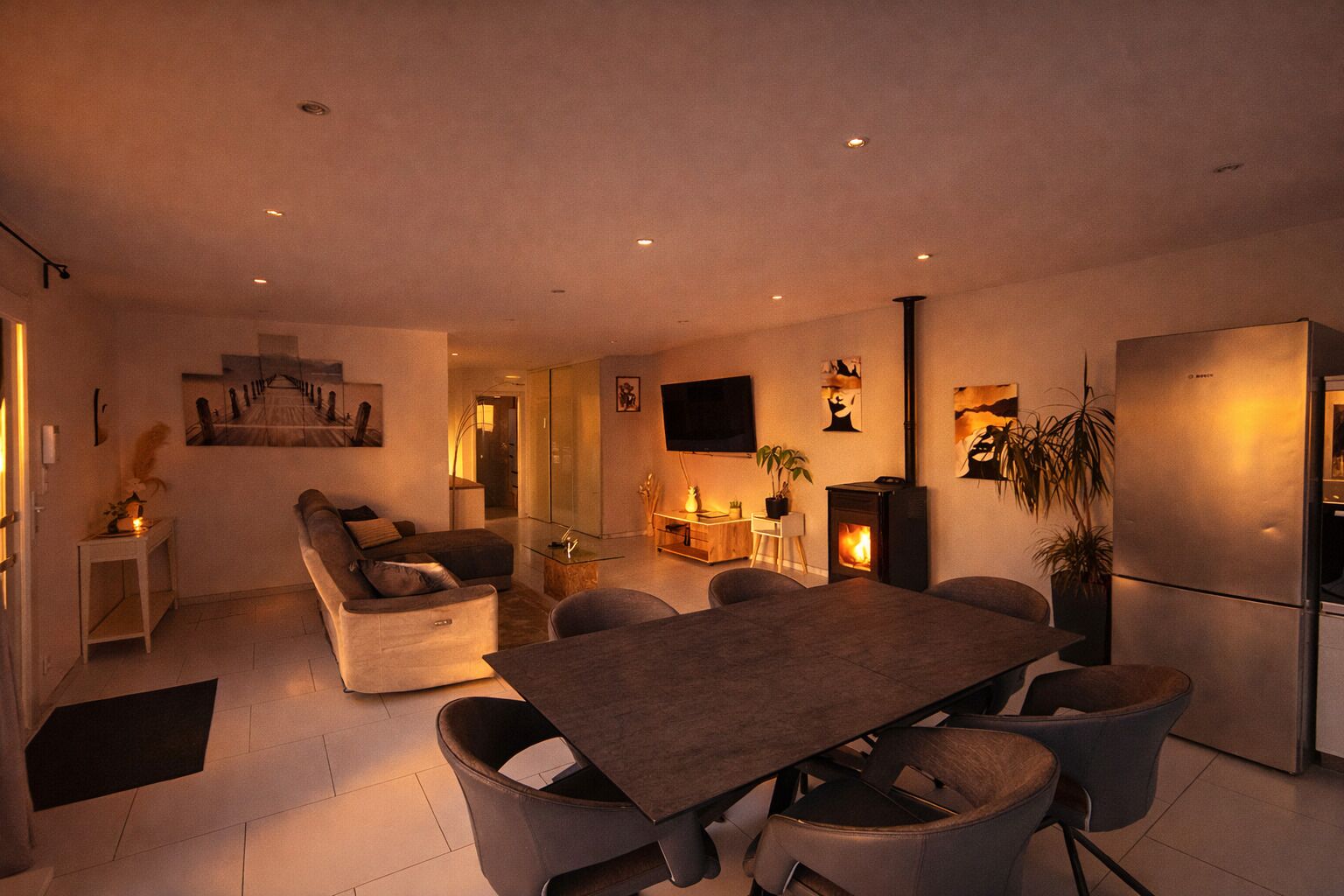 Uma sala de estar moderna com sofá, mesa de jantar com cadeiras, televisão de tela plana e lareira embutida.
