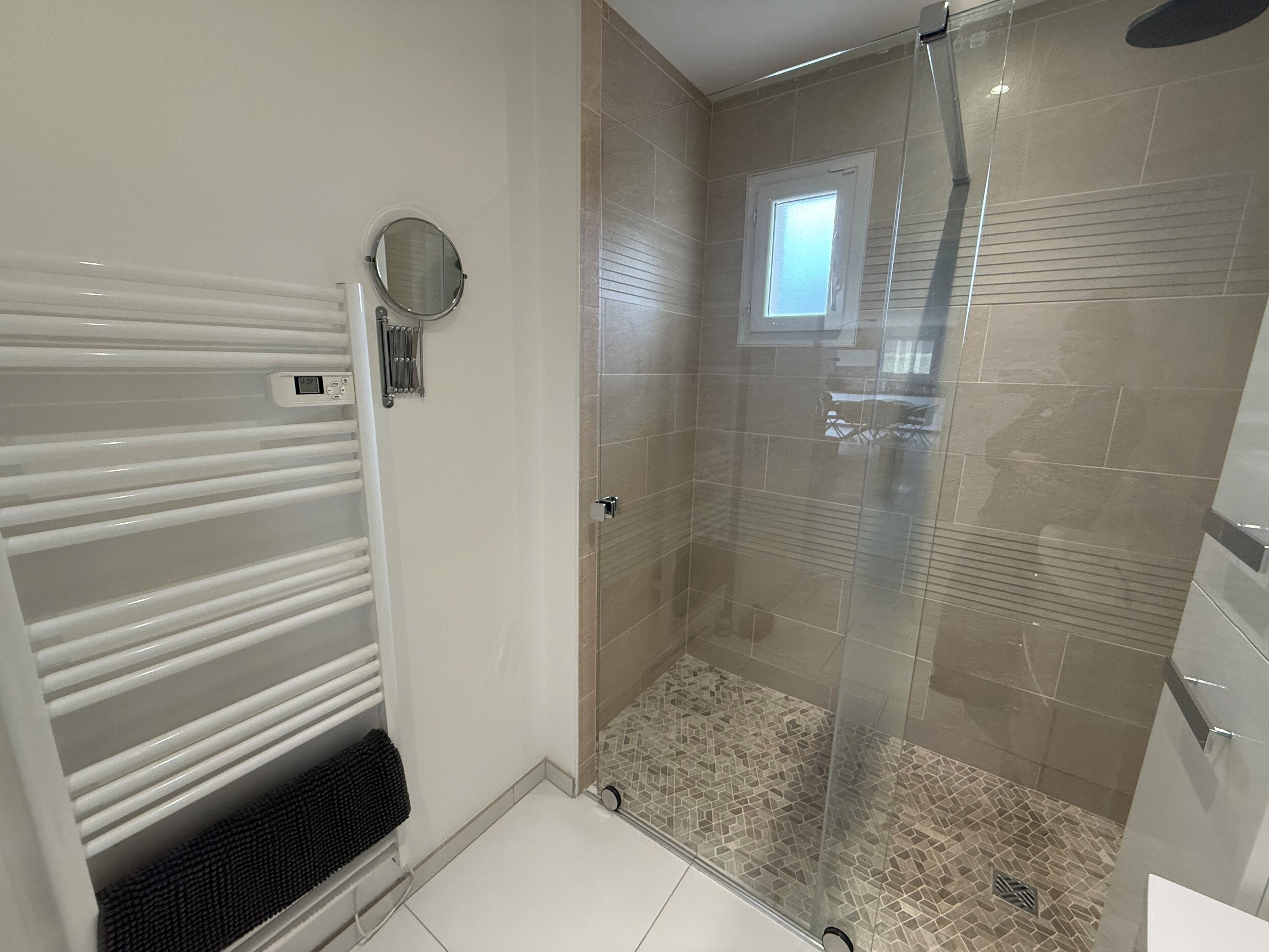 Ein modernes Badezimmer mit Duschkabine aus Glas, einem weißen Handtuchhalter und einem kleinen Fenster.