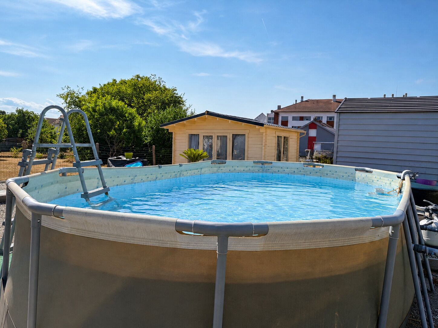 Ein oberirdischer Swimmingpool mit einer Leiter, umzäunt und von Bäumen umgeben.