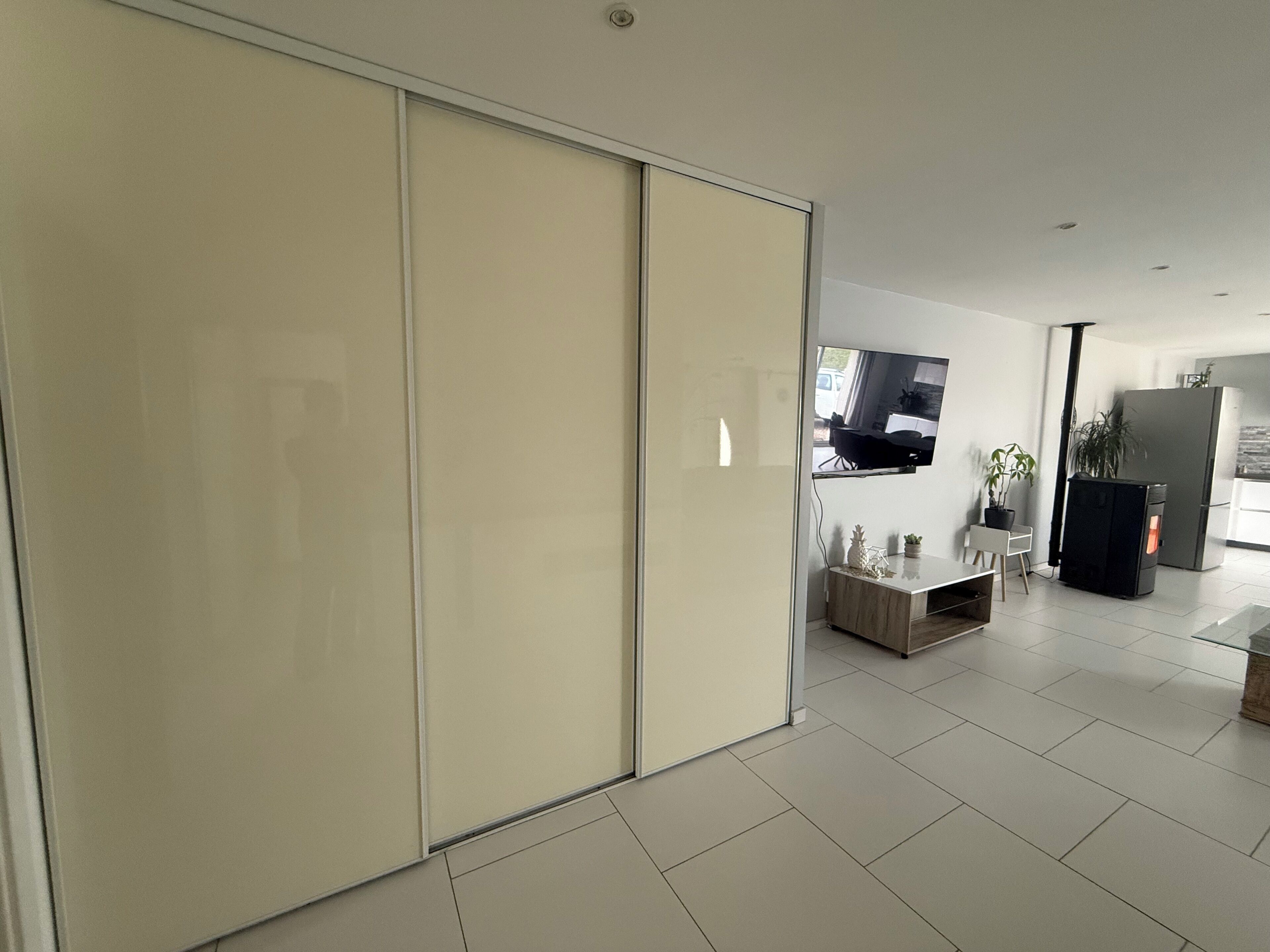 Een moderne woonkamer met een schuifdeur, een flatscreen televisie aan de muur, een eethoek met een tafel en stoelen, en een keuken met een koelkast en fornuis.