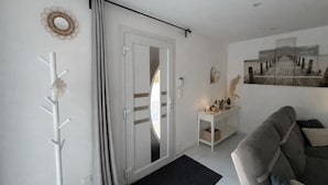 Una sala de estar moderna con un sofá gris, un perchero blanco, una mesita auxiliar con una vela y un cuadro colgado en la pared.