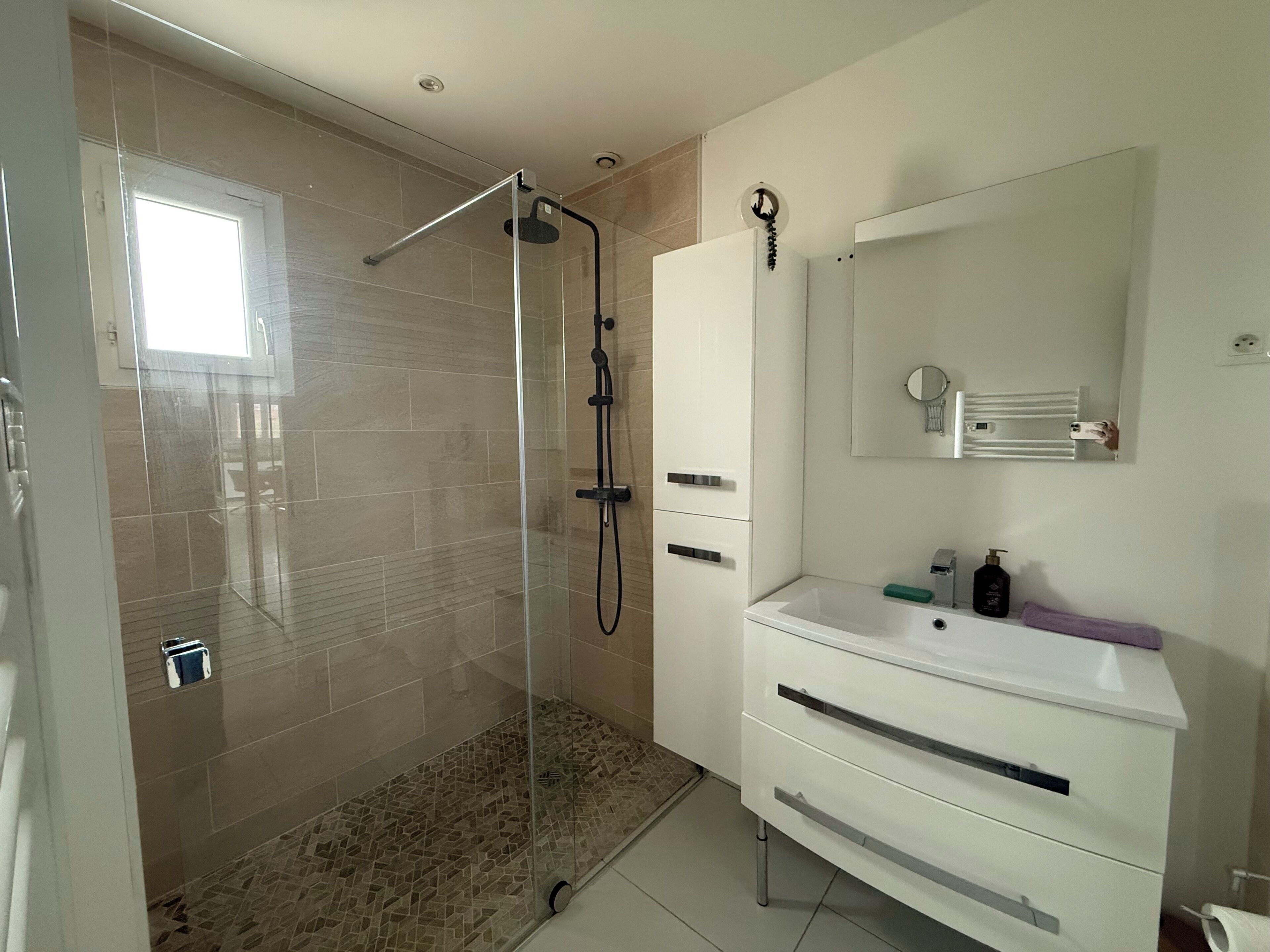 Une salle de bain moderne avec une douche à parois de verre, un meuble-lavabo blanc avec un miroir et un sol carrelé.
