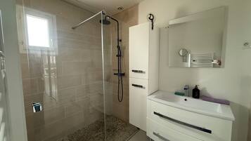 Une salle de bain moderne avec une douche à parois de verre, un meuble-lavabo blanc avec un miroir et un sol carrelé.