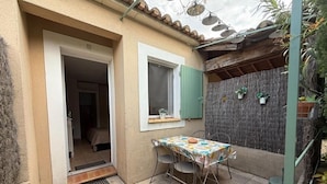 Un piccolo patio con tavolo e sedie, una porta che dà su una stanza e un muro decorato con piante in vaso.