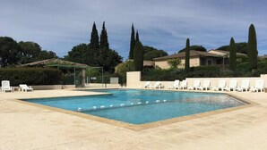 Una piscina rettangolare con bordo piastrellato, circondata da poltroncine bianche e un filare di alberi alti e slanciati.