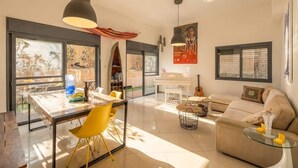 Un'ampia zona giorno con tavolo da pranzo, sedie gialle, divano, tavolino in vetro e pianoforte.