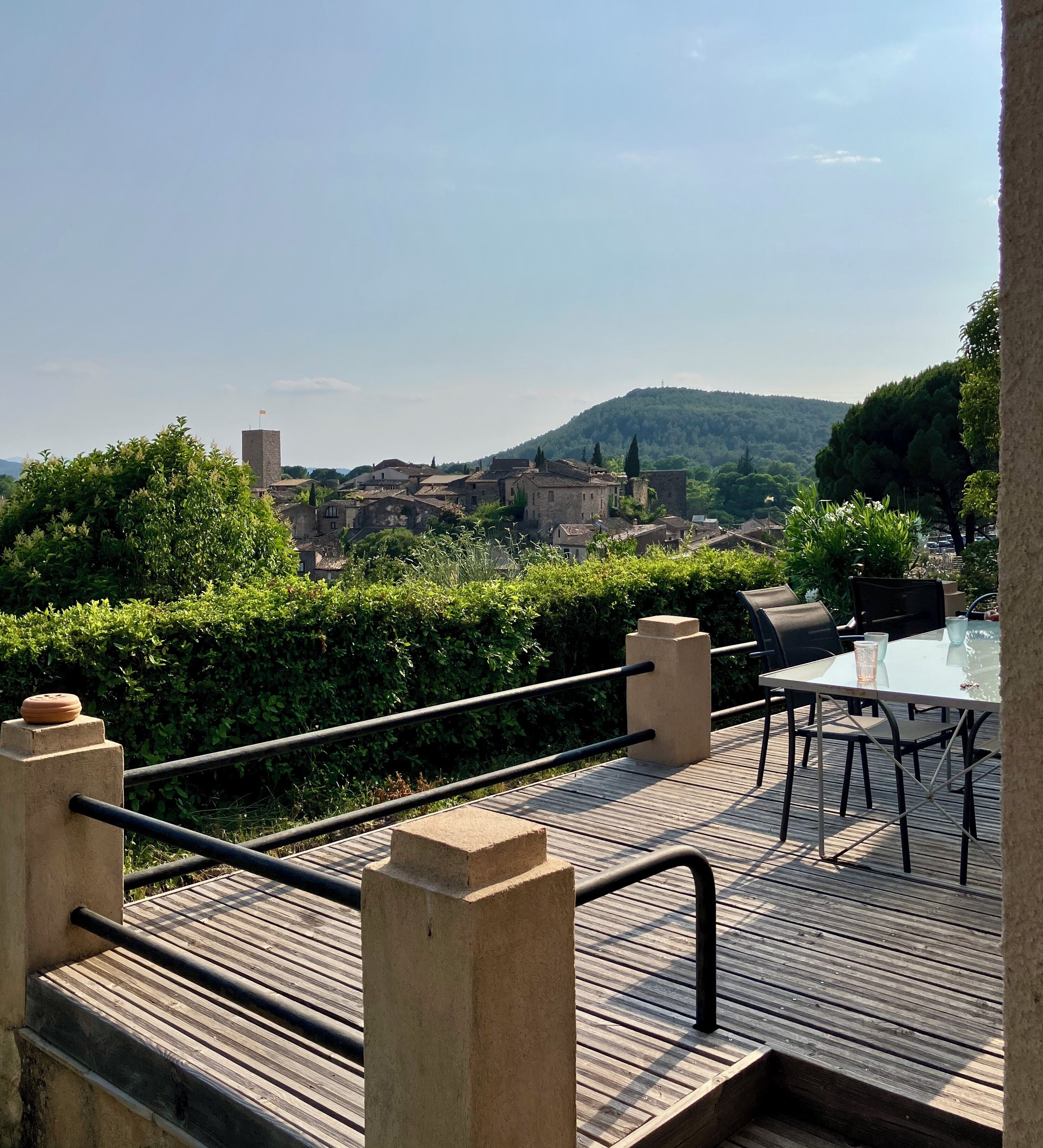 Une terrasse en bois avec une table et des chaises, offrant une vue sur une ville historique et une colline.