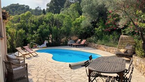 Area piscina con lettini, un tavolo in legno e una sedia in vimini.