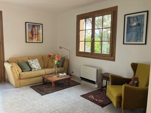 Un salon avec un canapé beige, une table basse en bois sur laquelle est posé un vase de fleurs, un fauteuil jaune et un radiateur.