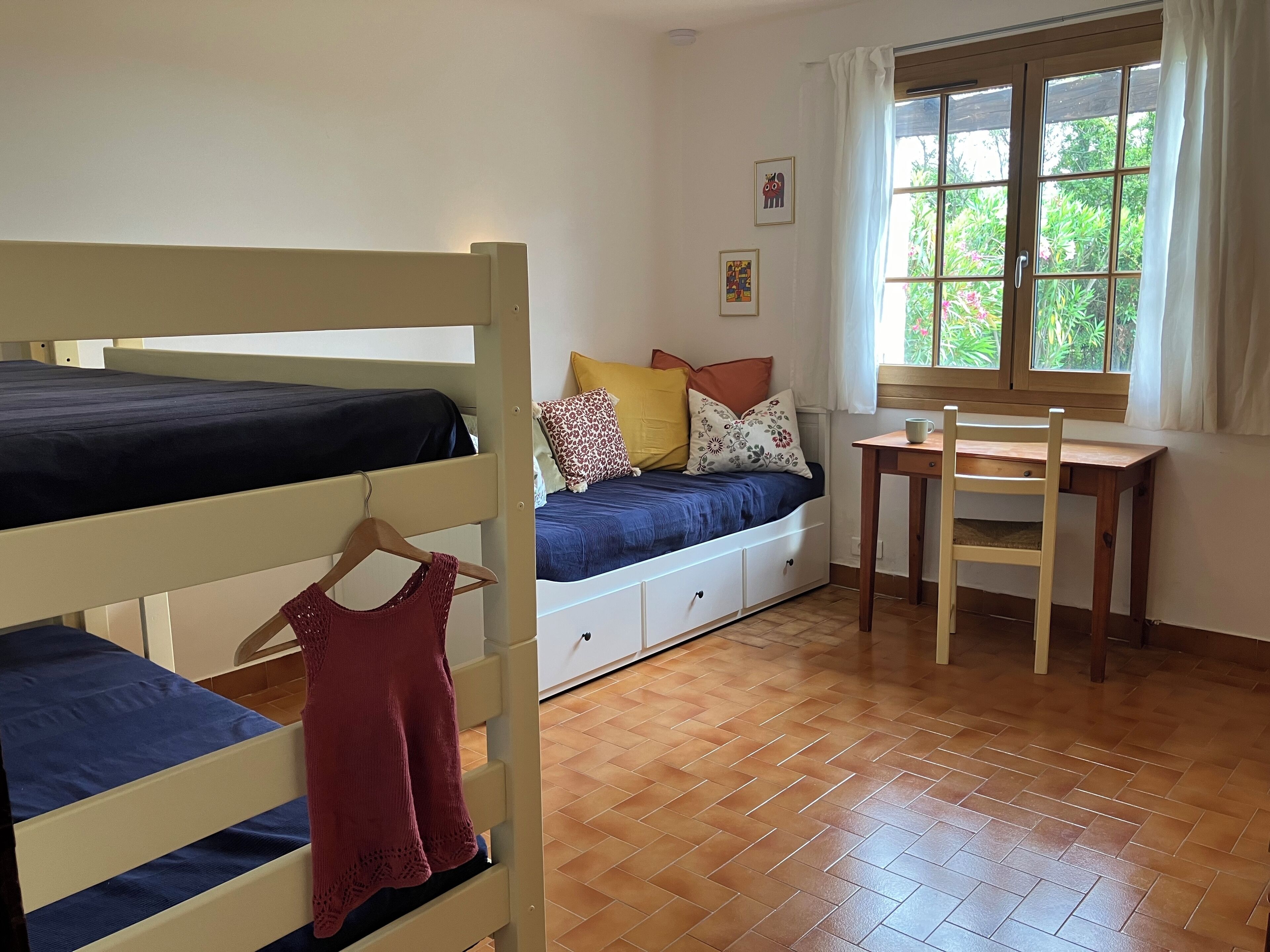 A dormitory room with bunk beds, a desk, and a window with curtains.